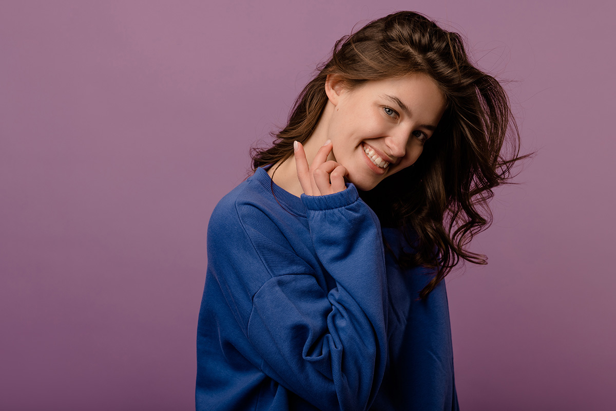 cute-young-caucasian-brunette-girl-blue-hoodie-looks-camera-purple-background-lifestyle-concept