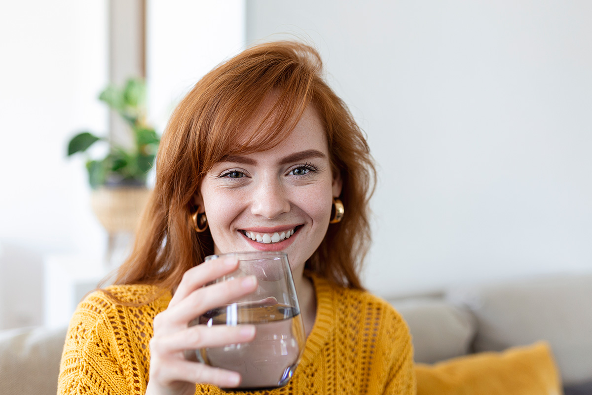 happy-young-woman-smiling-while-holding-glass-water-home