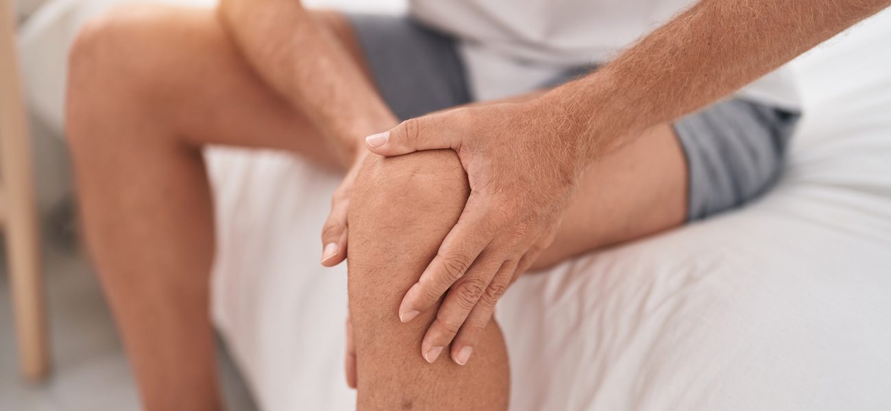 young-blond-man-suffering-knee-injury-sitting-bed-bedroom